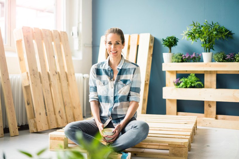 Femme assise dans un atelier entouré de palettes en bois.