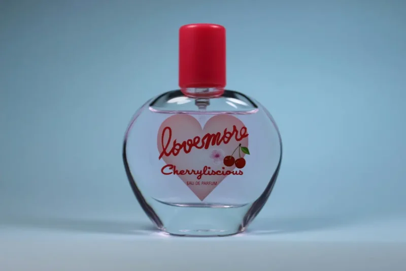 Flacon de parfum Lovemore Cherrylicious (eau de parfum) avec bouchon rose, sur fond bleu.