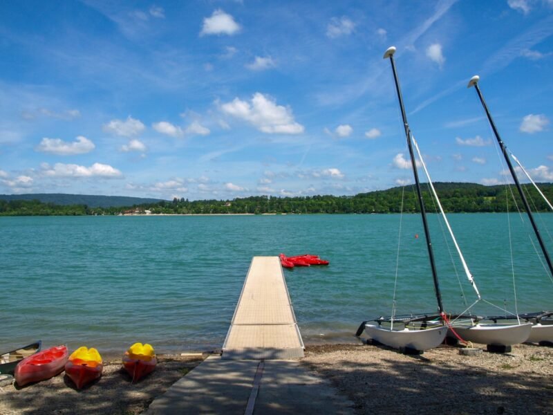 Kayaks et voiliers amarrés au bord d'un lac turquoise du Jura