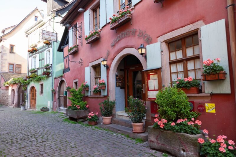 Rue pavée de Riquewihr bordée de maisons colorées et fleuries