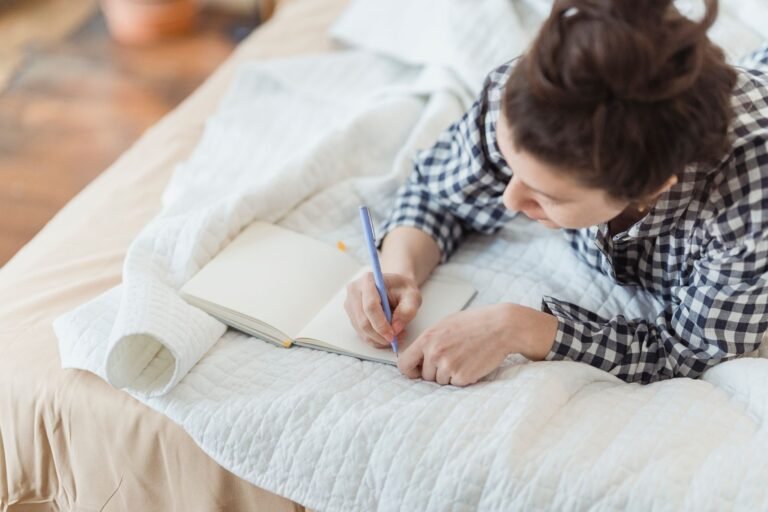 Femme écrivant dans un carnet, installée sur son lit
