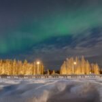Aurore boréale verte au-dessus d'une route enneigée bordée de bouleaux éclairés en Laponie finlandaise