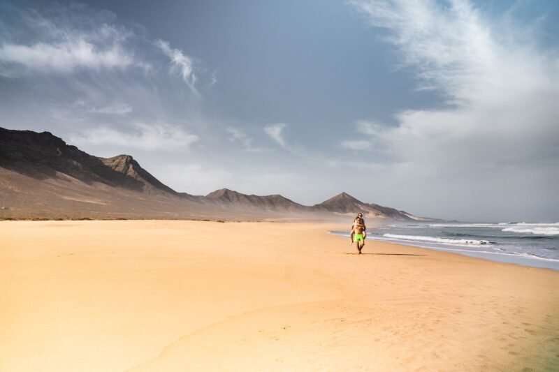 Personne marchant sur une grande plage de sable au pied des montagnes de Fuerteventura