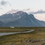 Une route sinueuse traverse une plaine verte au pied d'une montagne islandaise au crépuscule