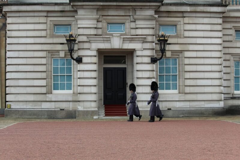 Deux gardes royaux en uniforme rouge et bonnet à poil défilant devant Buckingham Palace