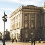Le Palais royal de Madrid baigné de soleil, avec des passants et des réverbères