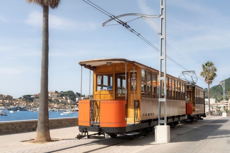 Le tramway en bois de Sóller longe la promenade du port de Sóller, la baie et ses bateaux en arrière-plan