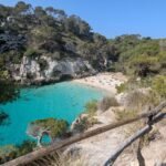 Crique aux eaux turquoise bordée de falaises et de pins à Minorque, vue depuis le sentier