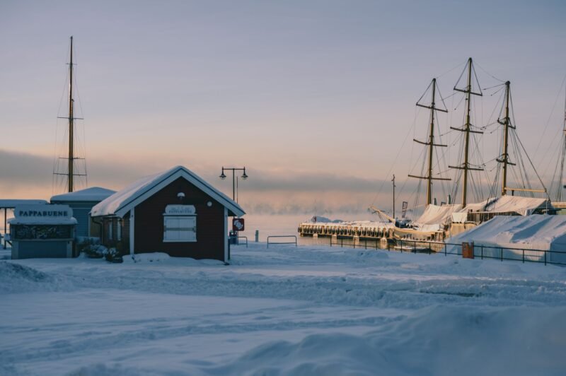 Le port d'Oslo enneigé en hiver, avec un voilier à quai et une cabane rouge au bord du fjord