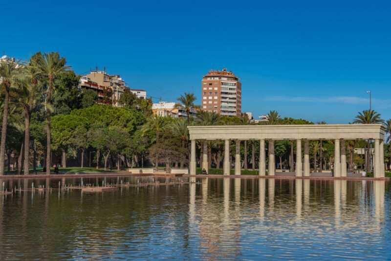 Une colonnade au bord d'un bassin dans le jardin du Turia à Valence, entourée de palmiers sous un ciel bleu